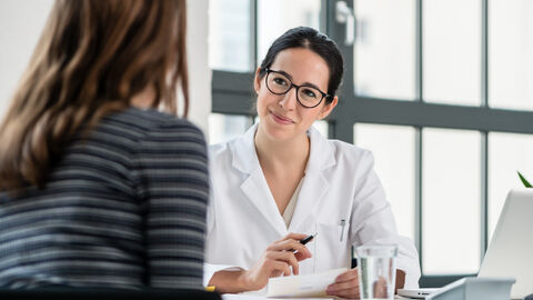 Eine Ärztin an einem Schreibtisch mit einer Patientin im Beratungsgespräch.
